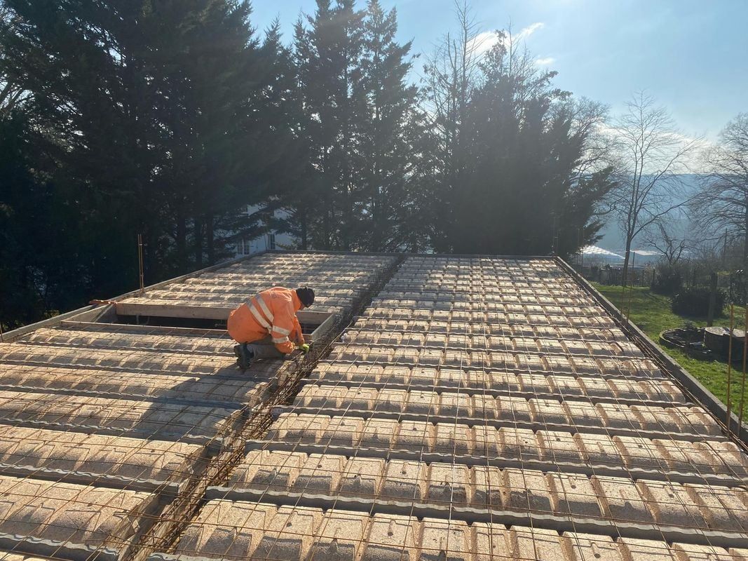 Un ouvrier du bâtiment, vêtu d'un gilet orange, installe des armatures en acier.