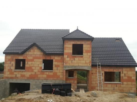 Une maison partiellement construite, en briques rouges avec un toit de tuiles.
