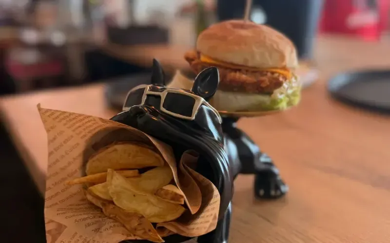 Figura de perro negro en una mesa con dos hamburguesas y papas fritas en conos de waffle.