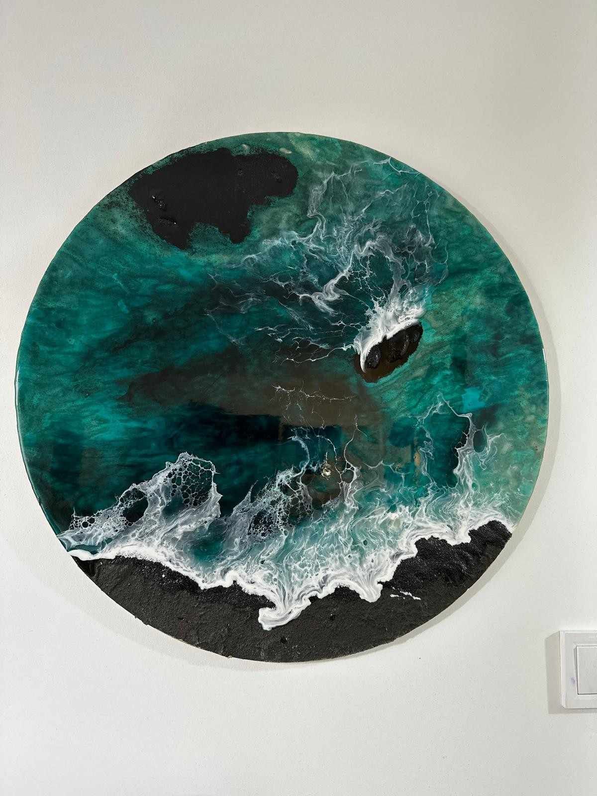 Obra de arte abstracta circular de color verde azulado y negro con textura blanca ondulada sobre una pared blanca.