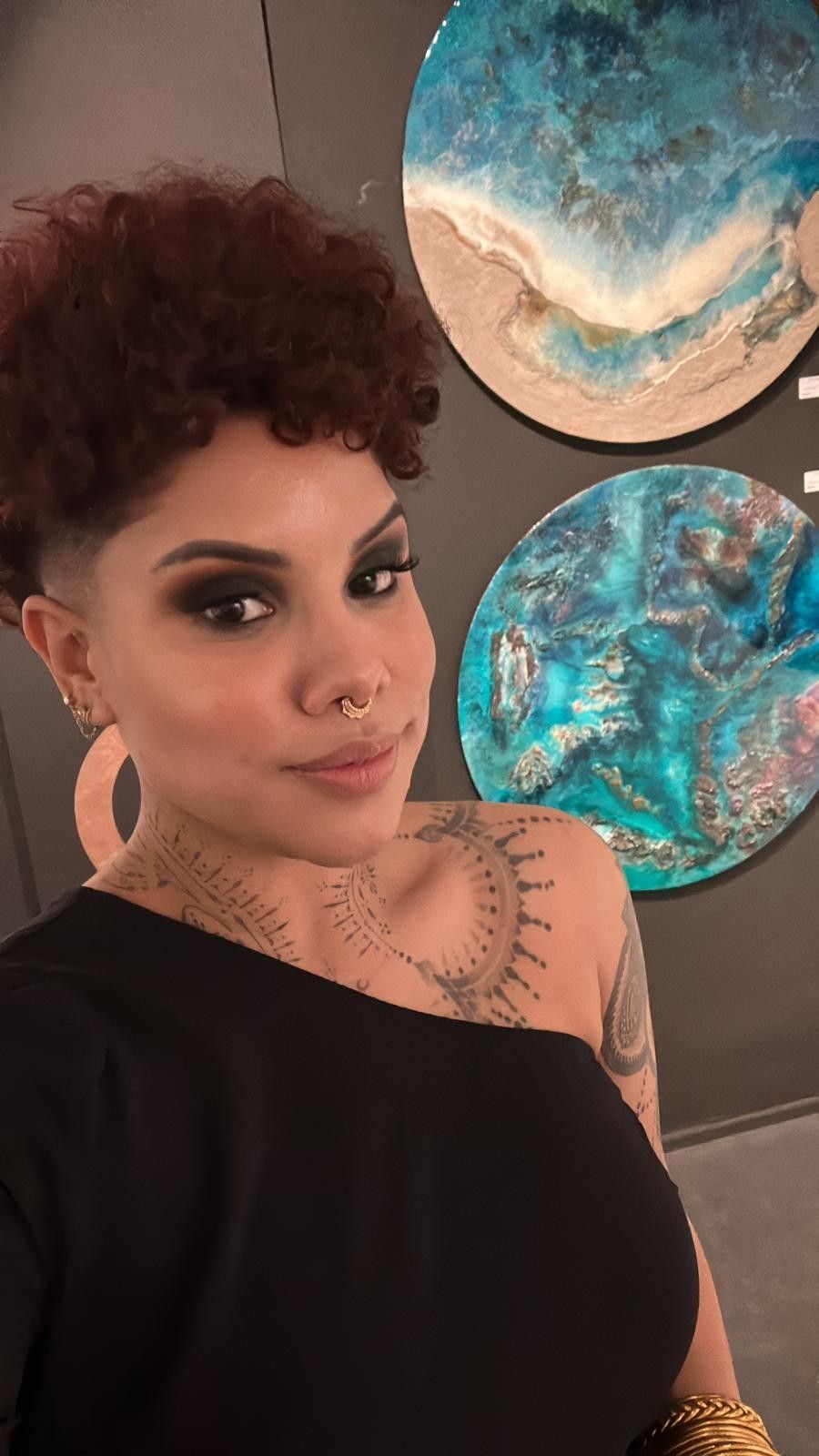 Mujer con blusa negra posando en el interior junto a dos coloridas obras de arte circulares en la pared.
