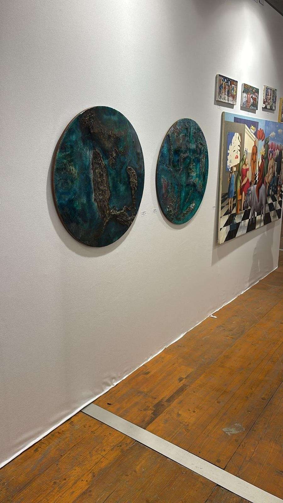 Pared de galería de arte con dos cuadros ovalados de color azul verdoso