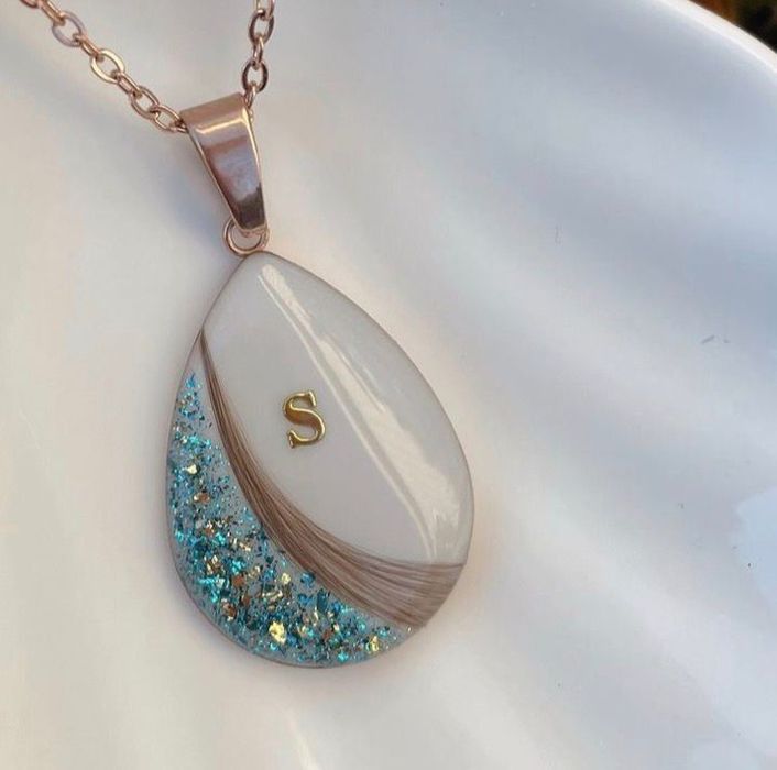 Collar con colgante en forma de lágrima, resina con purpurina blanca y azul y una inicial "S" dorada.