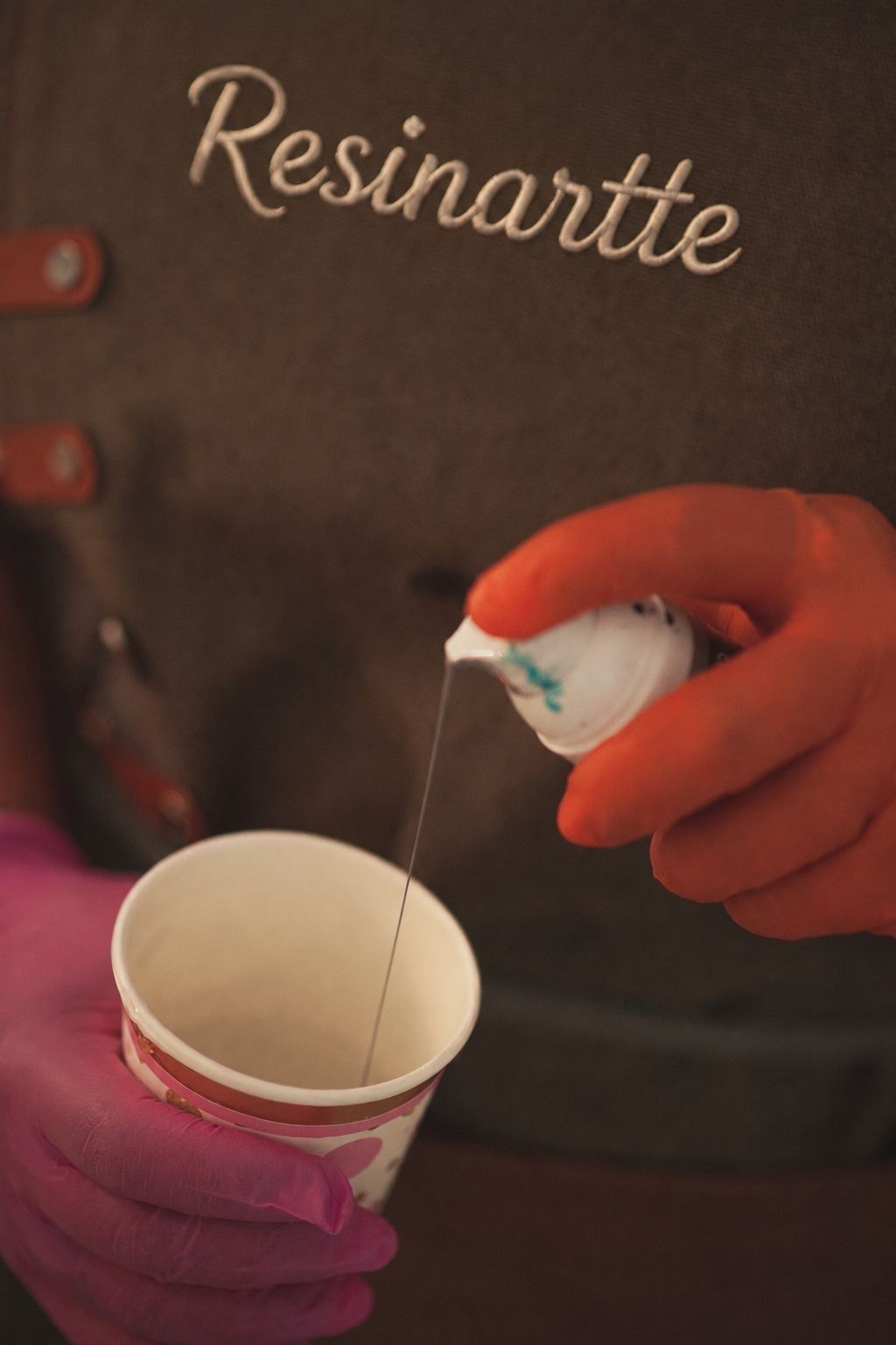 Vertiendo resina blanca a mano en una taza pequeña desde una botella exprimible con una mano enguantada de morado.