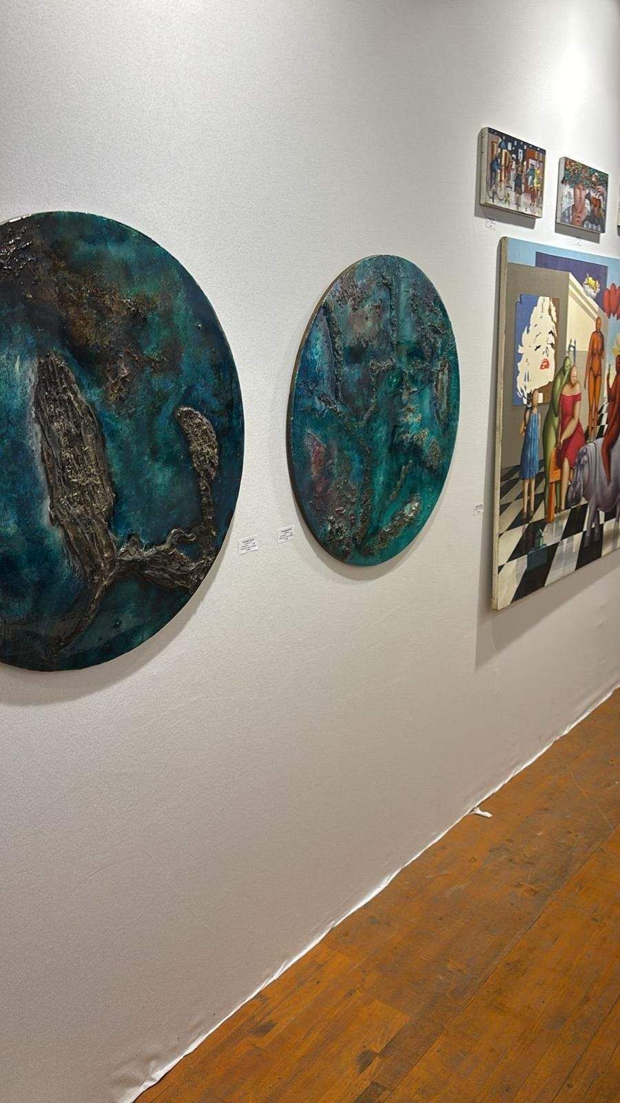 Pasillo de galería de arte con esculturas circulares de color verde azulado 