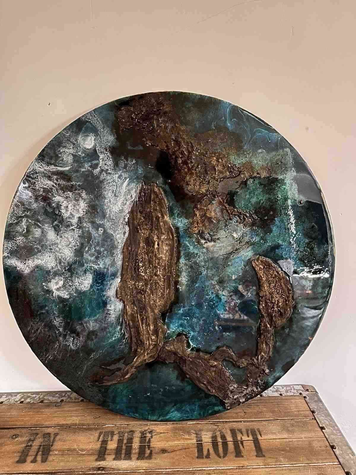 Obra de arte circular de técnica mixta que representa dos ballenas en tonos 