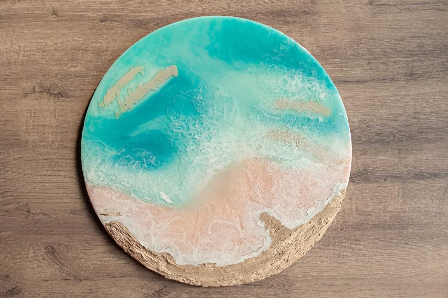 Posavasos redondo con temática playera, con diseño de resina en tonos turquesa y beige arena sobre una superficie de madera.