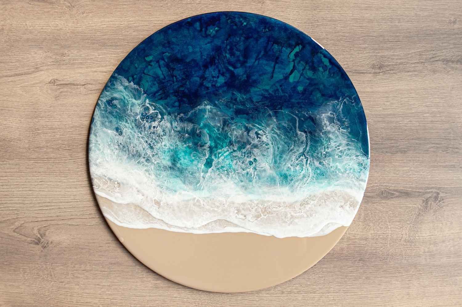 Ilustración circular de una escena playera con olas oceánicas de color turquesa y espuma blanca sobre un fondo color arena.