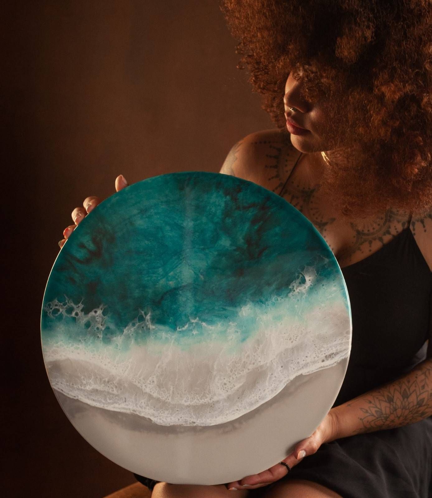 Mujer sosteniendo una pieza de arte redonda de resina con remolinos ondulados de color turquesa y blanco.