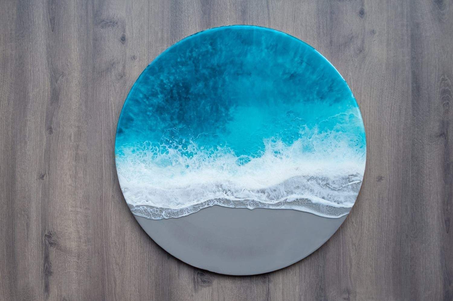 Pintura abstracta circular de paisaje marino en tonos azules y grises sobre una pared de madera.