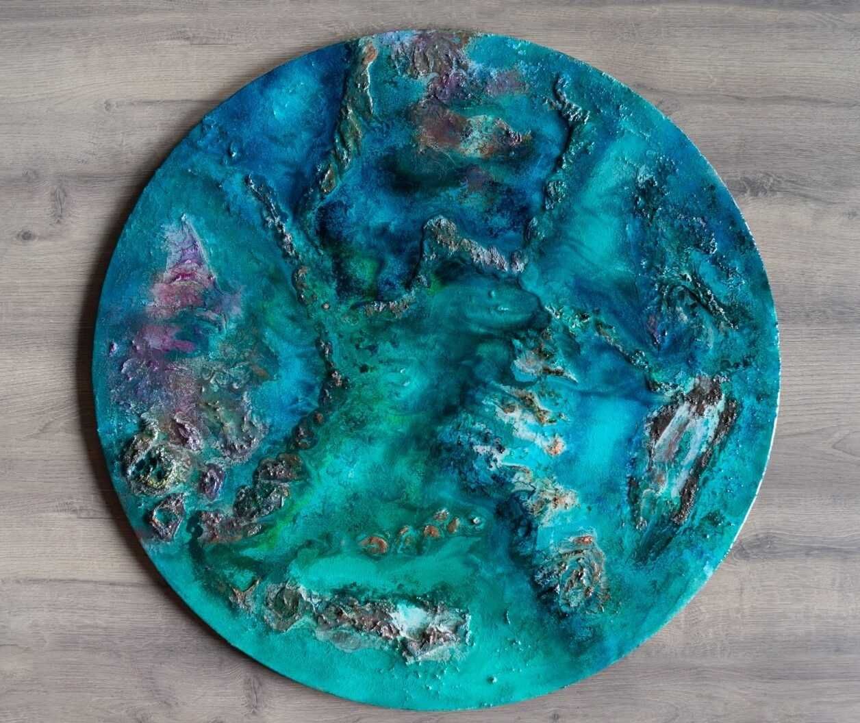 Obra de arte circular abstracta texturizada en tonos verde azulado y turquesa sobre un fondo gris.