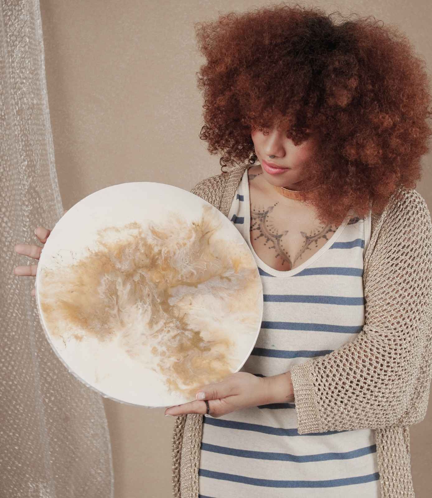 Mujer sosteniendo una pintura abstracta circular en una habitación con iluminación tenue.