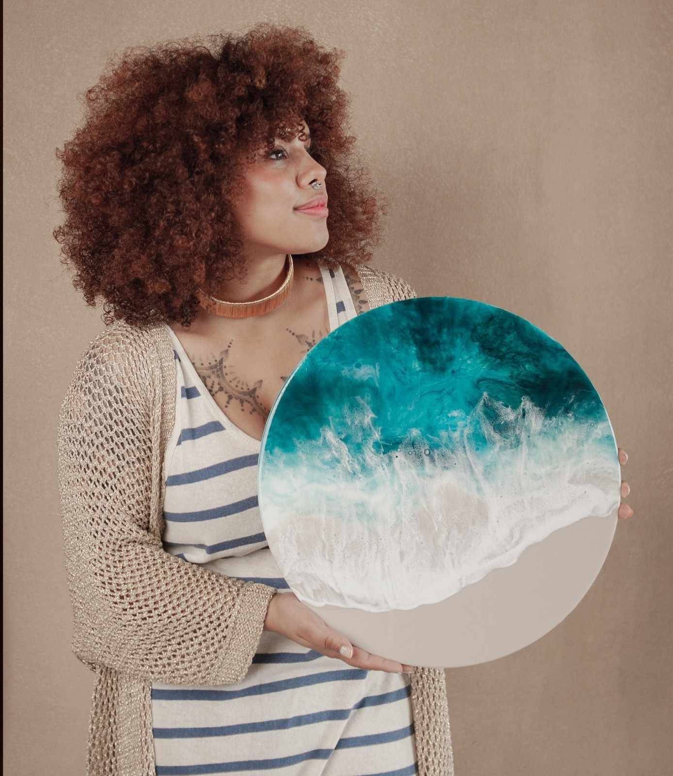 Mujer sosteniendo una lámina circular con una escena de playa sobre un fondo beige.