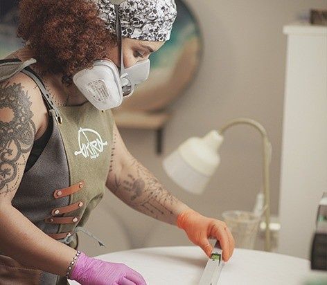 Artista con respirador y guantes, trabajando en una mesa con herramientas en un estudio.