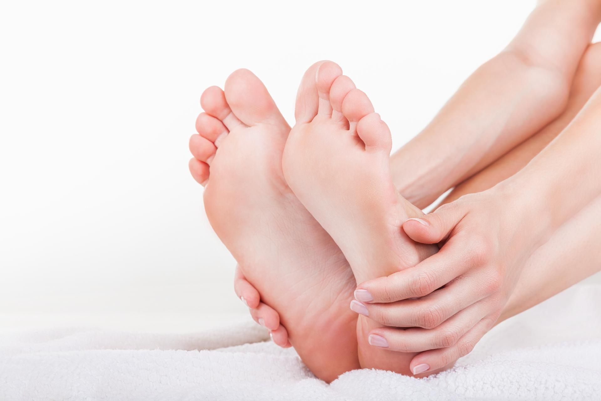 Hände, die nackte Füße umfassen und untersuchen, blasse Haut vor weißem Hintergrund.