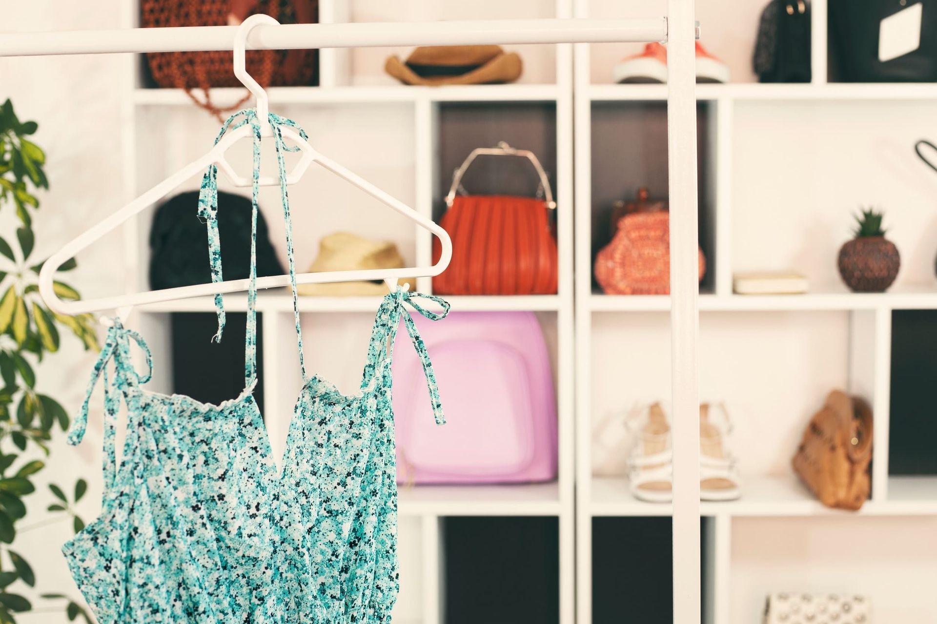 Un vestido floral azul cuelga de una percha delante de una estantería blanca llena de accesorios.