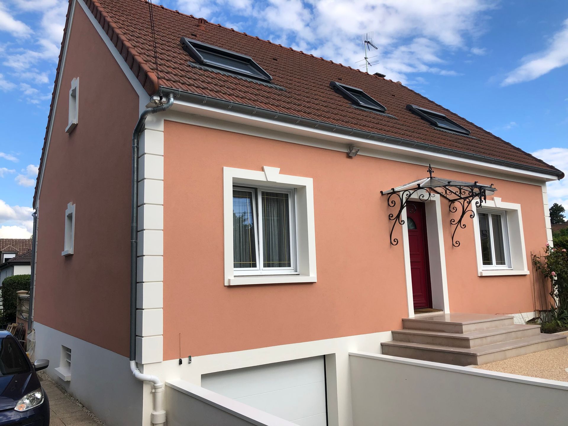 Maison couleur pêche avec des boiseries blanches, un toit rouge et des marches à l’entrée sous un ciel bleu