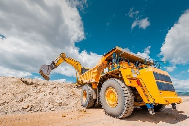 Un camión volquete amarillo está siendo cargado con tierra por una excavadora.