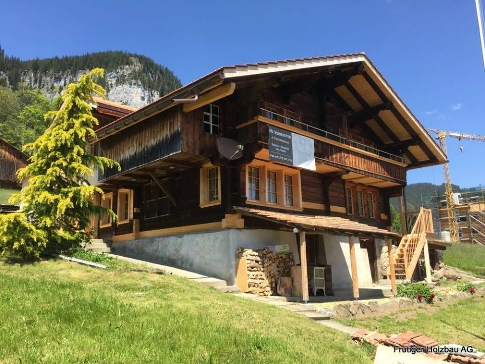 Ein hölzernes Chalet mit hellen Zierelementen vor einer bergigen Kulisse an einem sonnigen Tag.