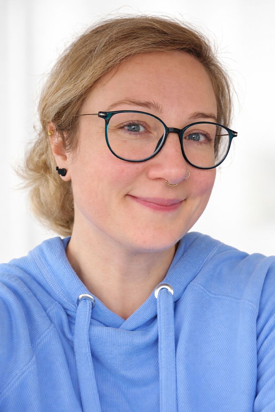 Eine Frau in weißem Hemd und grauer Weste lächelt in einem Restaurant.