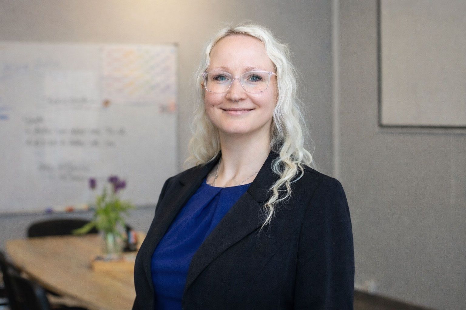 Frau mit Brille und weißem Blazer, die leicht lächelt.