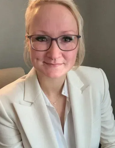 Frau mit Brille und weißem Blazer, die leicht lächelt.