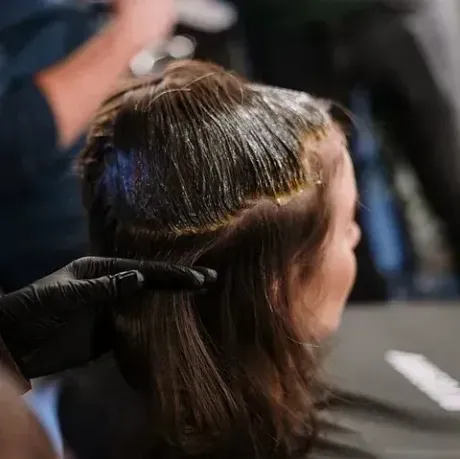 A una persona le están tiñendo el cabello en un salón de belleza; una mano enguantada aplica el tinte.