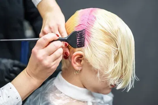 Persona con cabello rubio recibiendo la aplicación de tinte rosa en un salón de belleza.