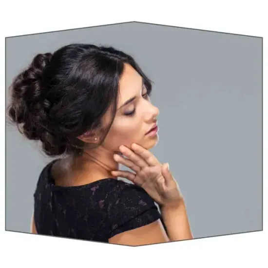 Mujer con cabello oscuro recogido en un moño, vestida con un vestido negro, se toca la mejilla, situada en un cubo gris.