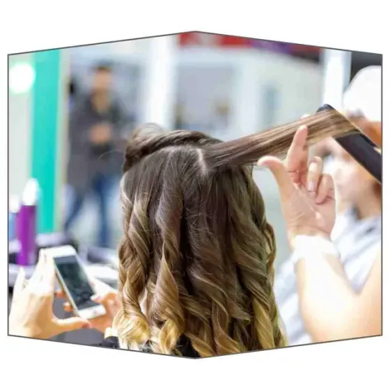 Estilista rizando el cabello de una clienta; persona tomando una foto con su teléfono en un salón de belleza.