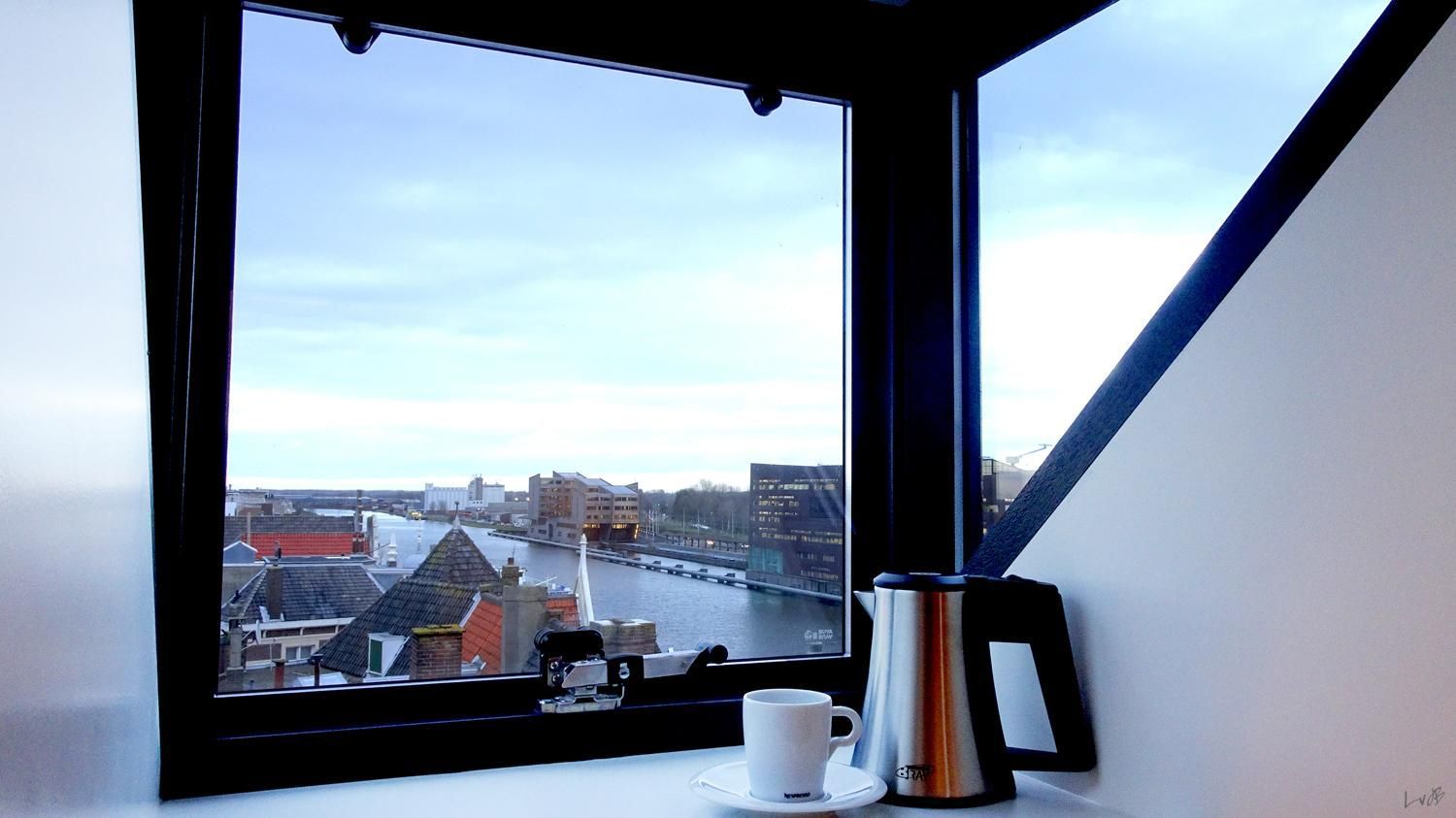 Een raam met uitzicht op een stad en een kopje koffie