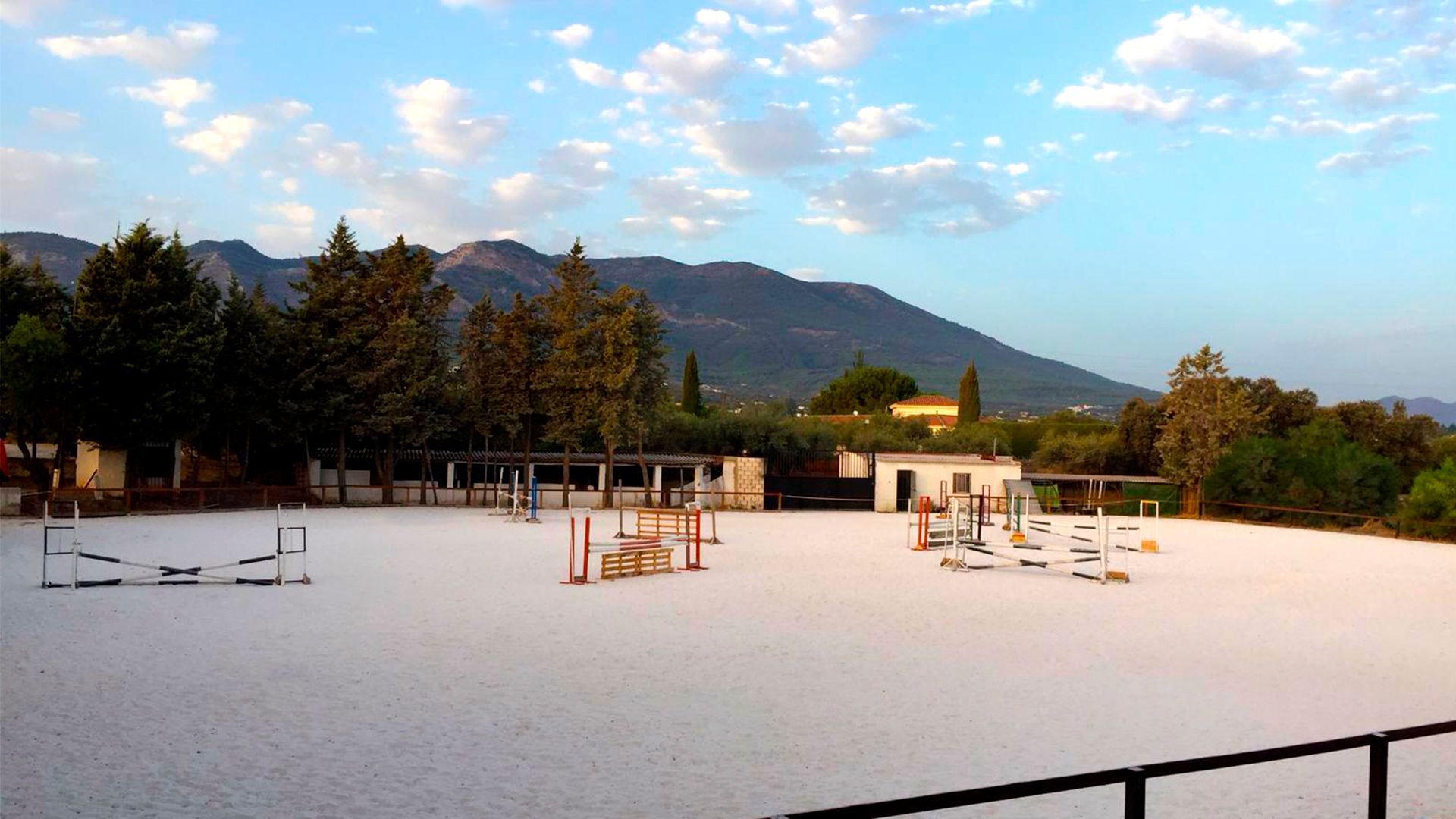 Parque infantil al aire libre con suelo blanco, columpios y estructuras para trepar, con árboles y montañas de fondo