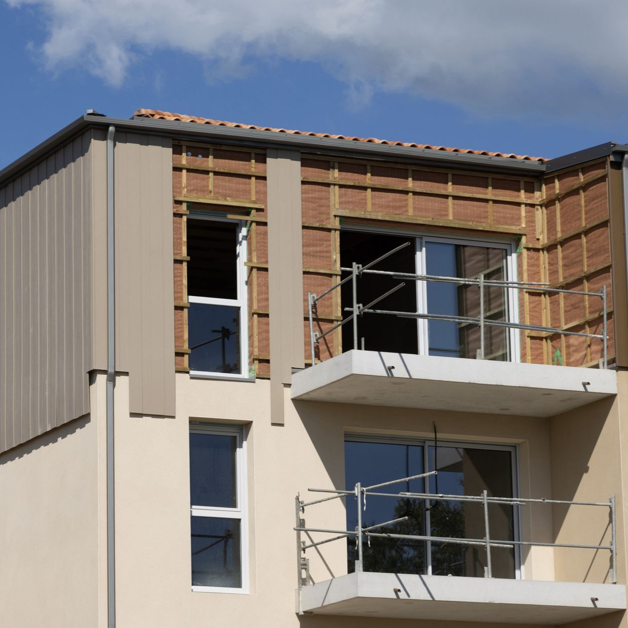 Bâtiment en construction avec balcon, façade inachevée et isolation brune.
