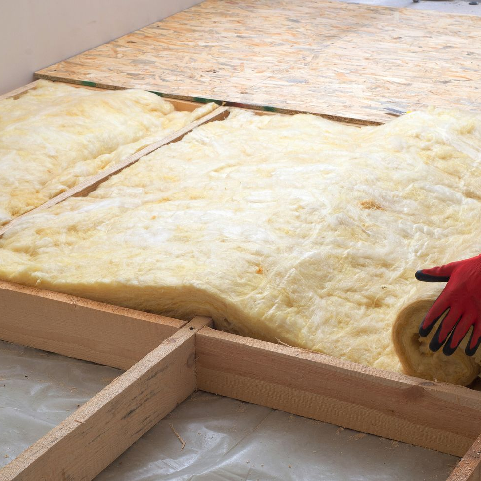 Installation d'isolant entre les solives du plancher en bois. Une main tient l'isolant.