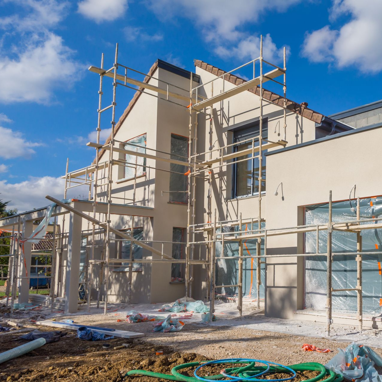 Maison en construction avec échafaudages contre des murs beiges.