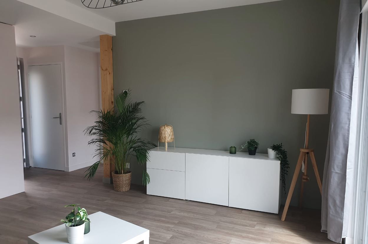 Pièce vide avec escalier en bois, murs blancs et sol gris.