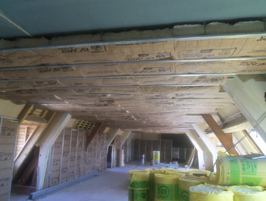 Salon lumineux et minimaliste avec murs blancs, parquet et canapé. Cuisine et escalier visibles.