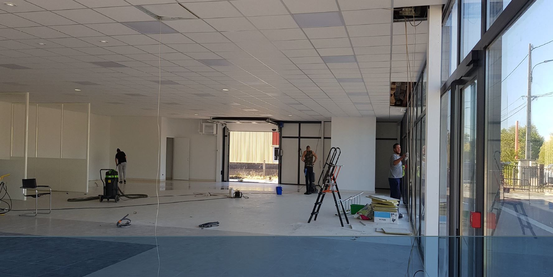 Pièce vide et lumineuse en cours de rénovation, pots de peinture au premier plan, échelle et vue sur la ville.