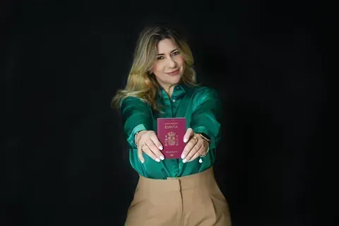 Una mujer con una camisa verde sostiene un pasaporte en sus manos.