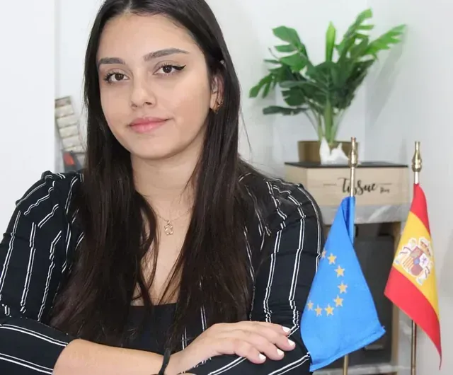 Una mujer con una camisa de rayas blancas y negras está parada frente a banderas.
