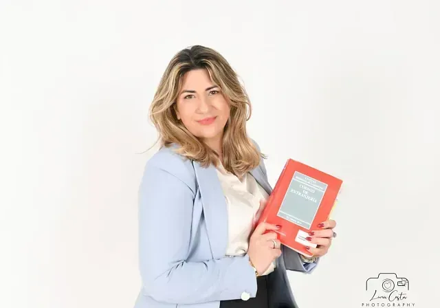 Una mujer con una chaqueta azul sostiene un libro rojo.
