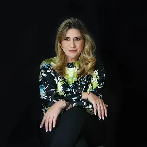 Una mujer con una camisa floreada está sentada en una silla con las piernas cruzadas.