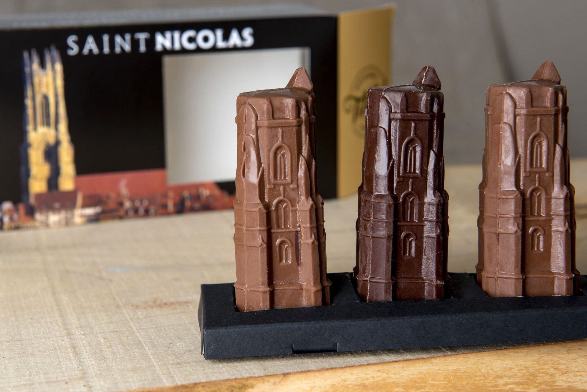 Trois figurines en forme de tour de chocolat, avec l'emballage de Saint Nicolas en arrière-plan.