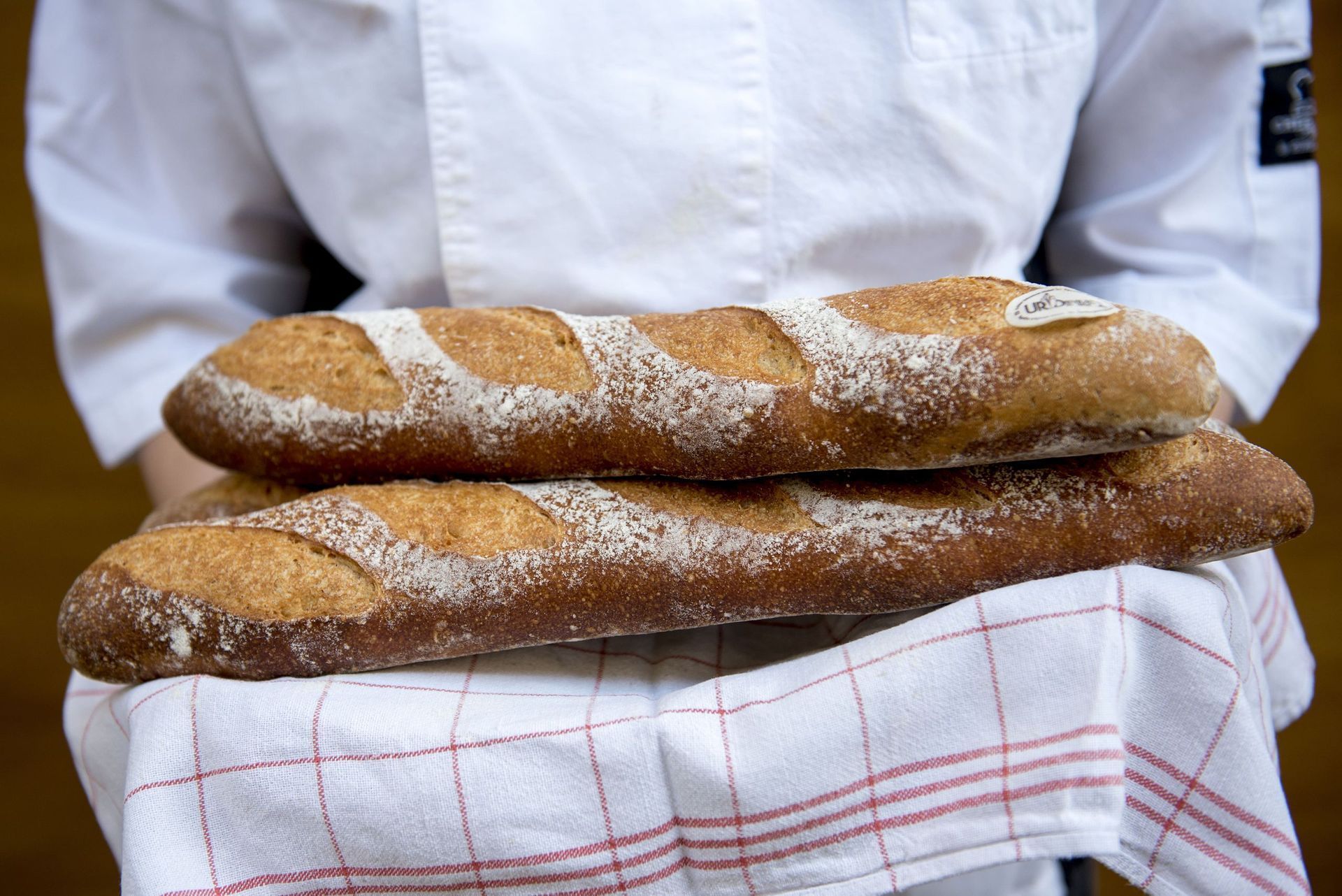 Boulanger tenant deux baguettes croustillantes sur une nappe à carreaux.