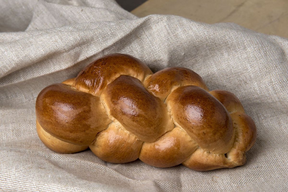 Pain challah doré tressé sur une nappe en lin beige.