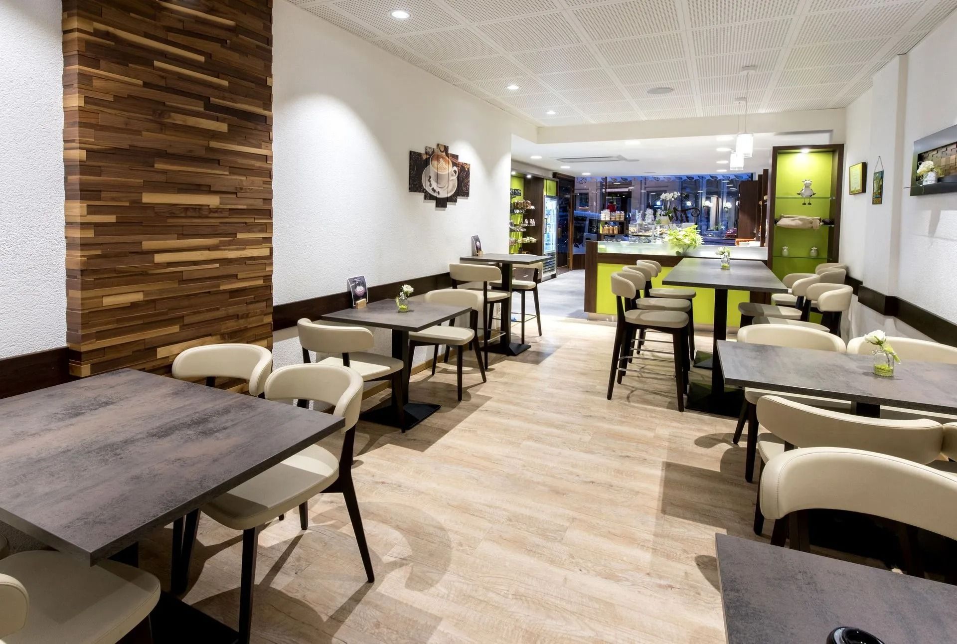 Intérieur de restaurant avec tables et chaises, mur d'accent en bois, parquet en bois clair et plafond texturé.