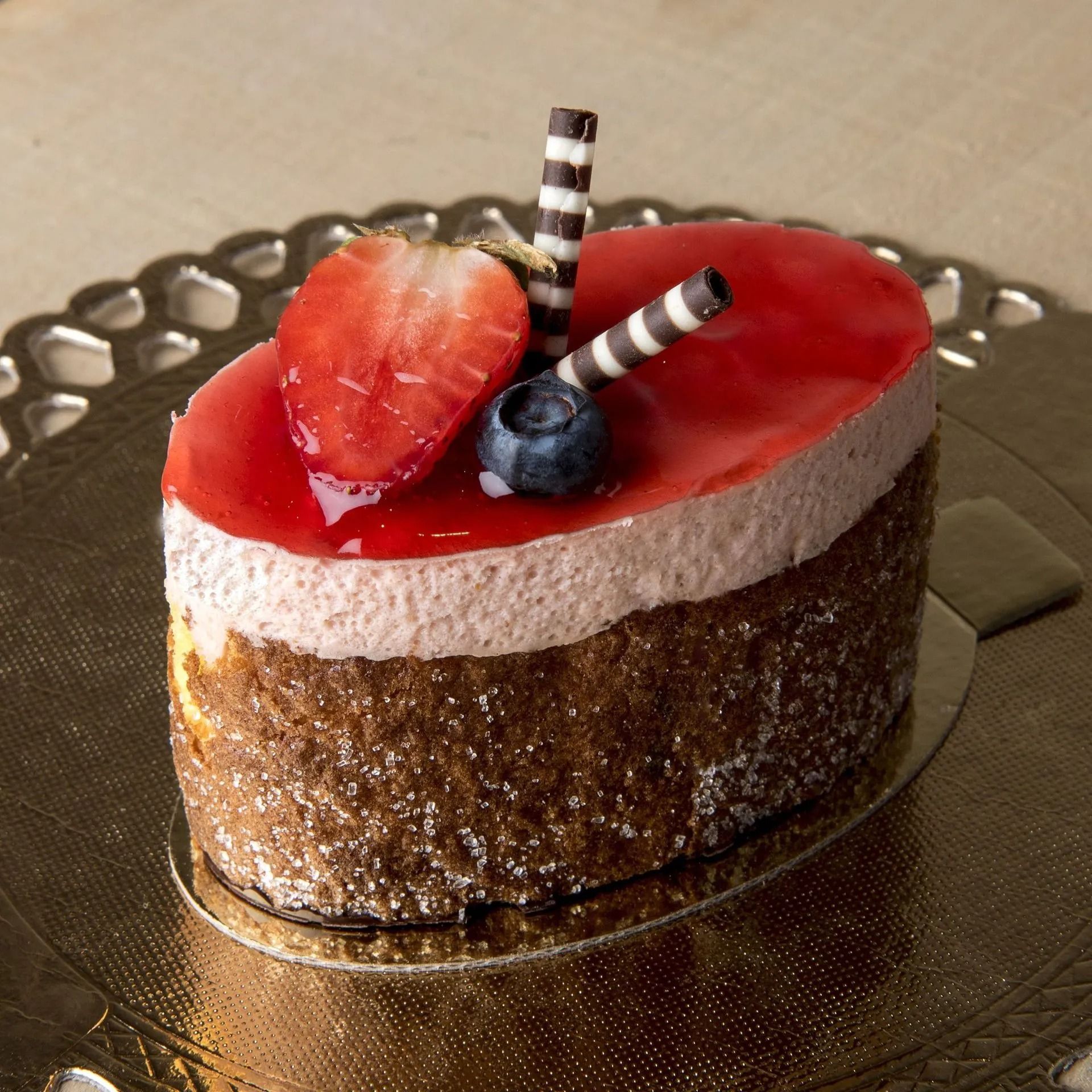 Gâteau aux fraises avec glaçage rouge, décoré d'une tranche de fraise, de myrtille et de bâtonnets de chocolat.