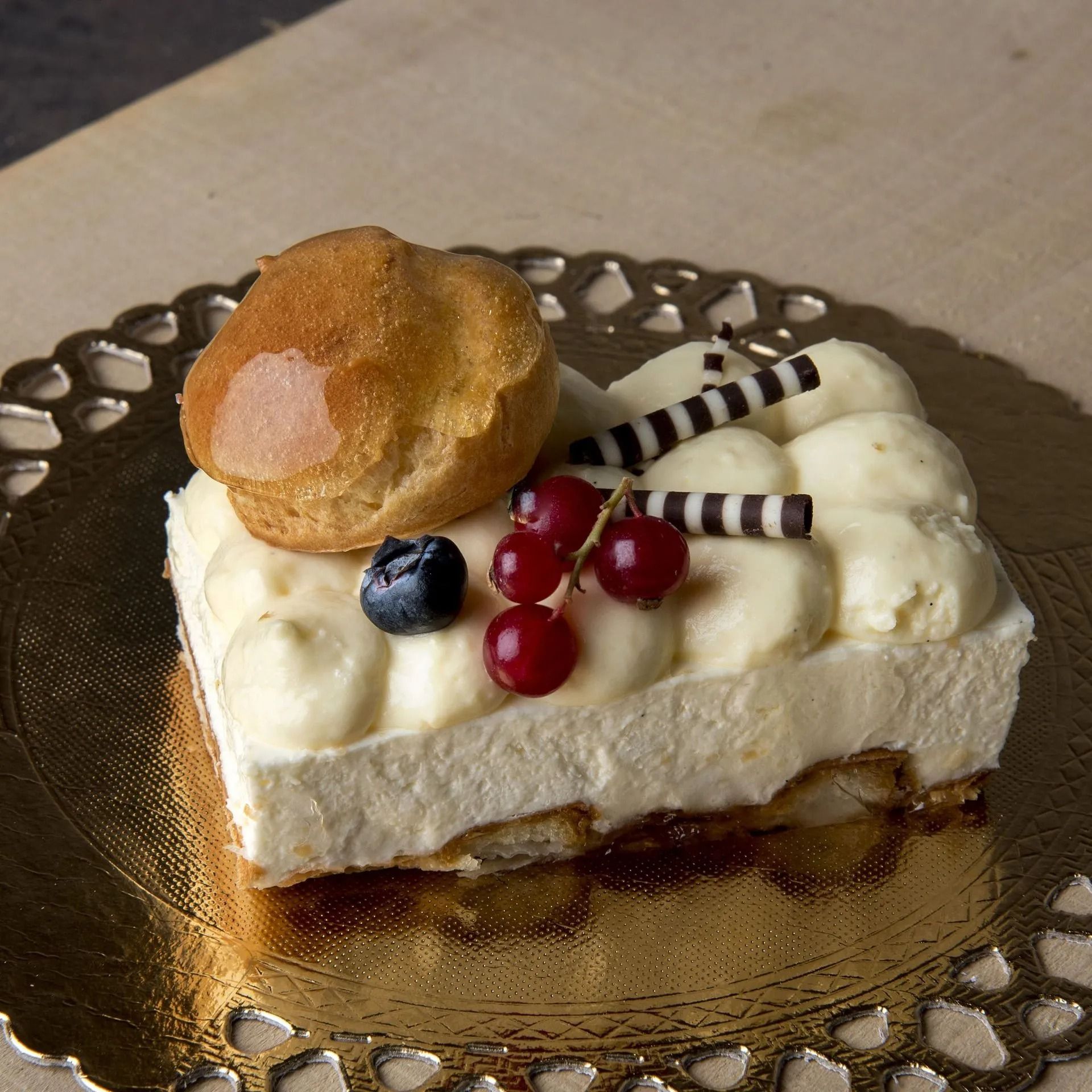 Gâteau avec garniture à la crème, baies, chocolat et chou sur une assiette dorée.
