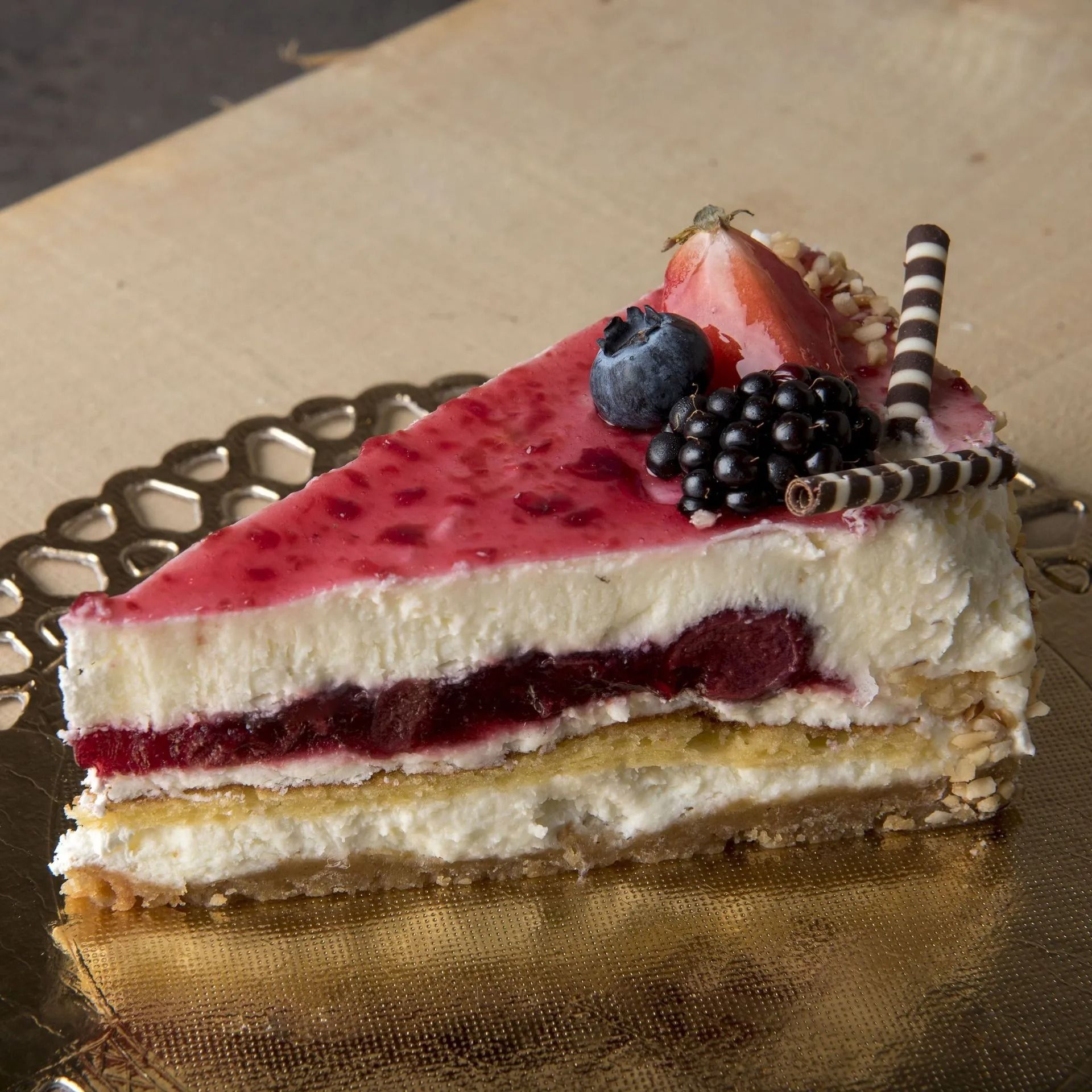 Tranche de cheesecake aux baies avec un glaçage rouge, garnie de baies et de copeaux de chocolat.