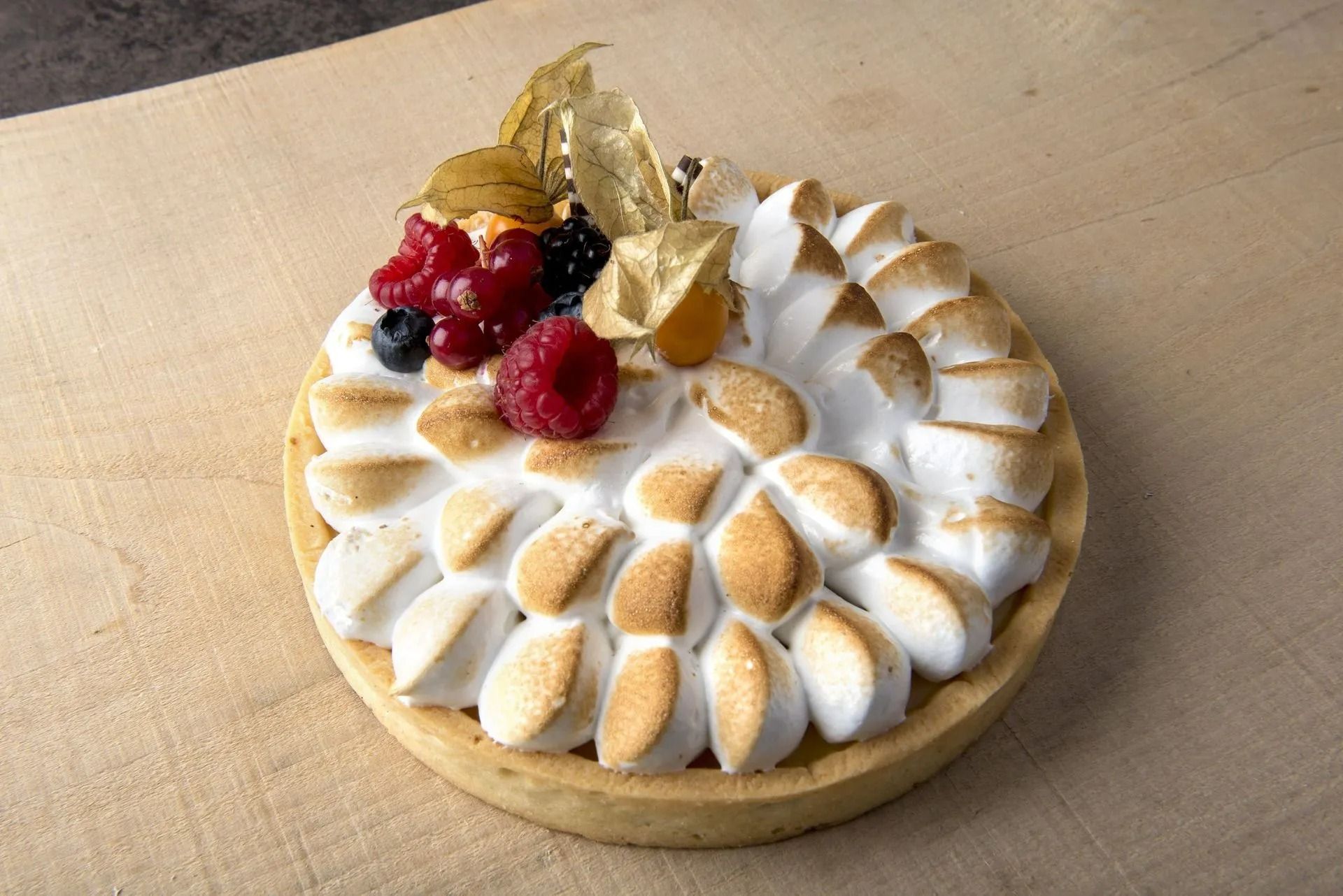 Tarte au citron meringuée garnie de baies et de cerises dorées.